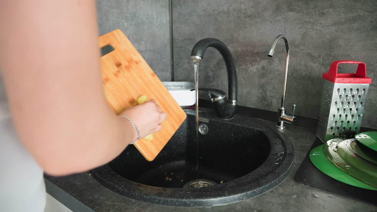 Hands scrubbing narrow wooden kitchen tool under running tap water in black sink, highlighting attention to cleanliness, hygiene, care for utensils, and detail-oriented domestic routine in modern kitchen space