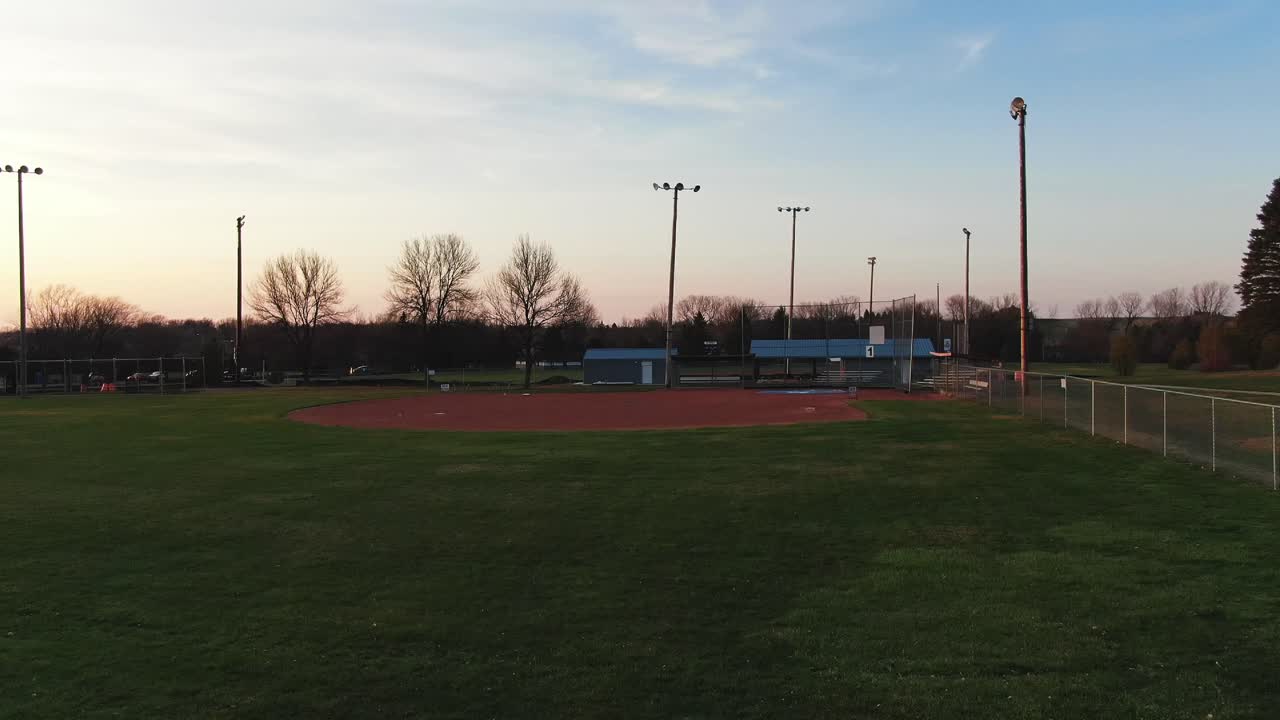 Aerial drone forwarding shot over a green park during with a baseball and soccer field on a sunny summer evening time