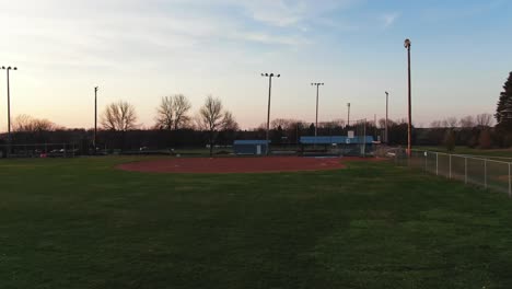 aerial drone forwarding shot over a green park during with a baseball and soccer field on a sunny summer evening time