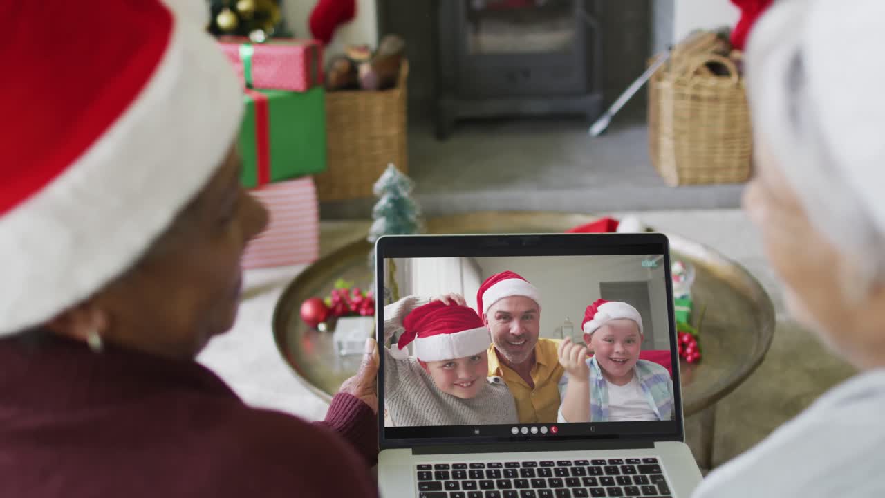 dos amigas mayores diversas que usan una computadora portátil para una videollamada de navidad con la familia en la pantalla