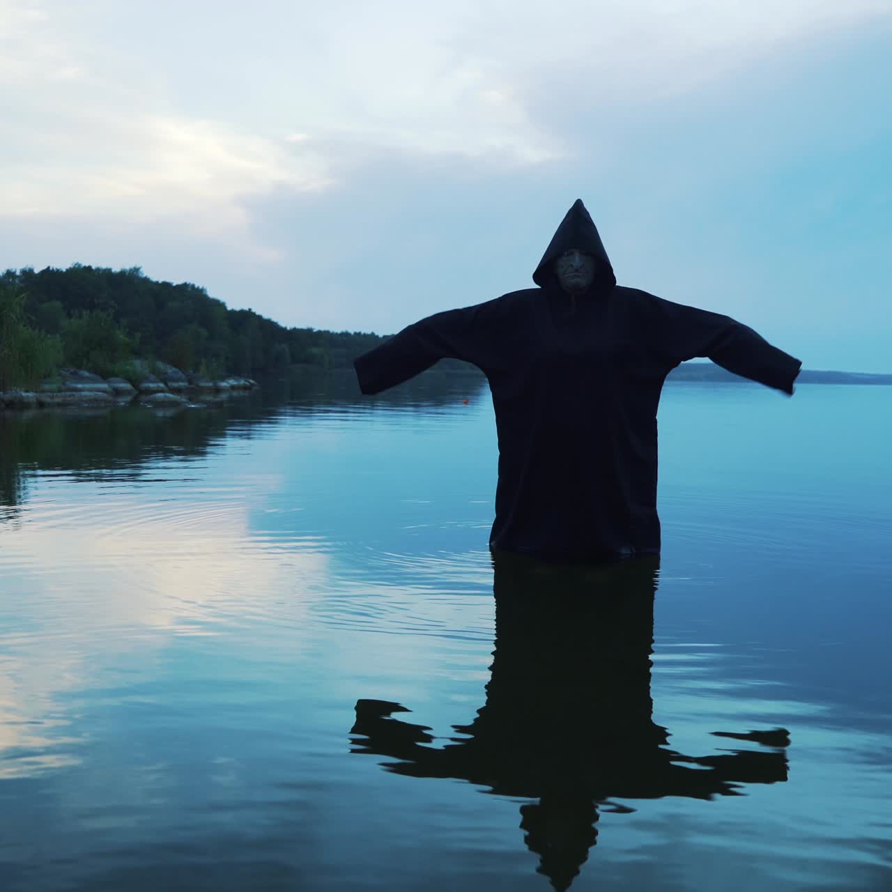 Scary figure in black mantle in the river. Halloween costume.