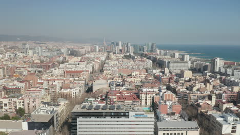 Fly-above-city,-heading-towards-modern-urban-borough-with-tall-skyscrapers.-City-lined-by-sea-coast.-Barcelona,-Spain