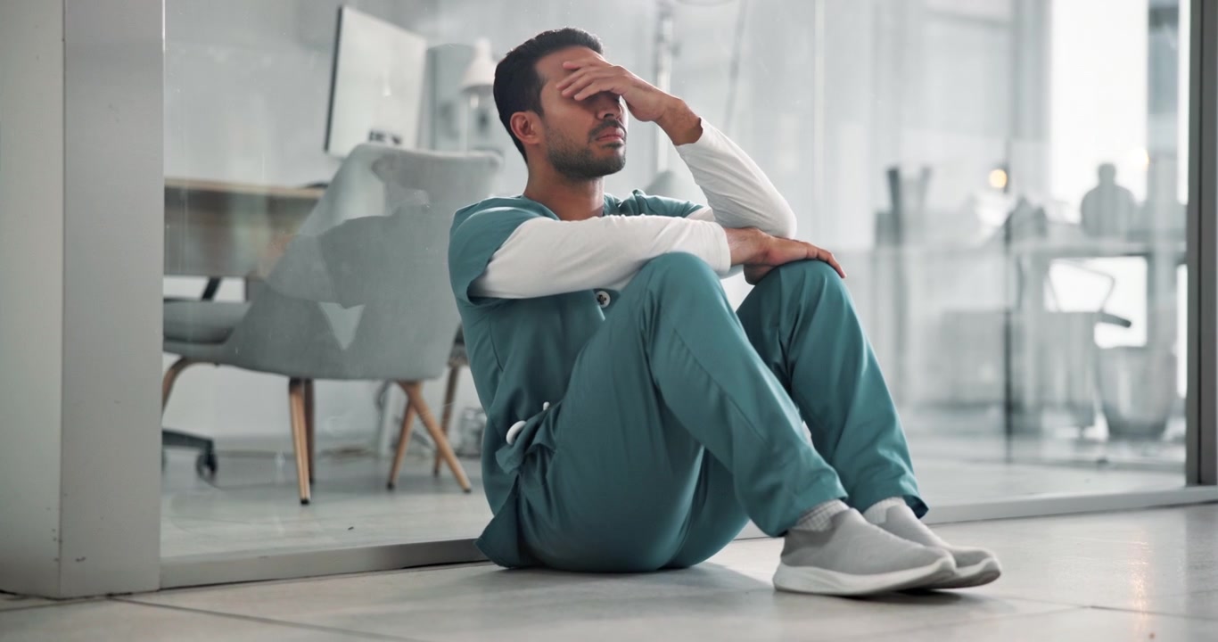 Stressed Male Healthcare Worker Sitting on Floor in Hospital