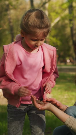 mother shows large butterfly to curious little daughter in shady spring park. woman and girl observe flying bug. environmental education in town