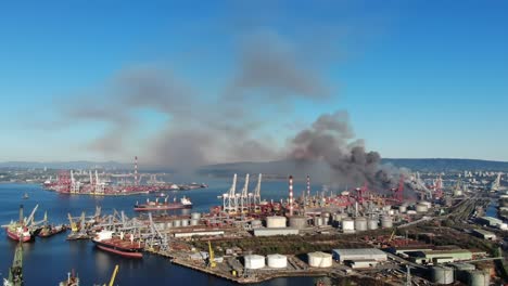 aerial view of industrial port scene with smoke erupting from nearby facilities, boats and cranes dot the landscape under clear blue skies