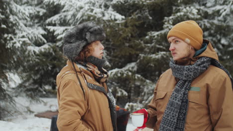 tourists chatting over tea at campsite in winter forest