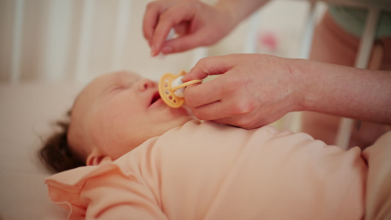 Close up of a baby lying down while a caregiver gently cleans the nose and holds a pacifier