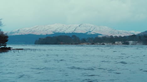 tracking shot from boat of lake surrounded by snow in winter