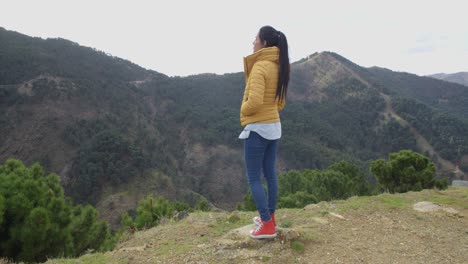 Woman-in-yellow-coat-near-mountain-valley