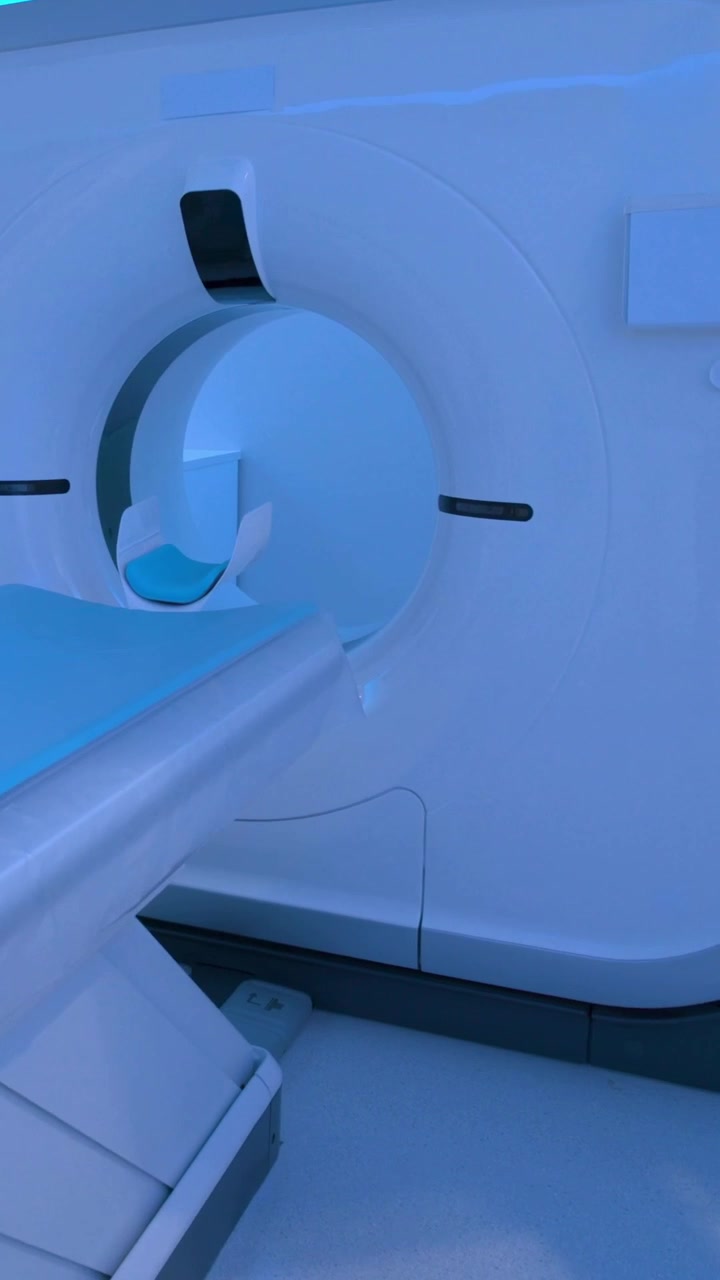 Video verticale: Avvio di una TAC nella sala di scansione, con il tavolo che scorre nel gantry, LED verde e cuscino blu.