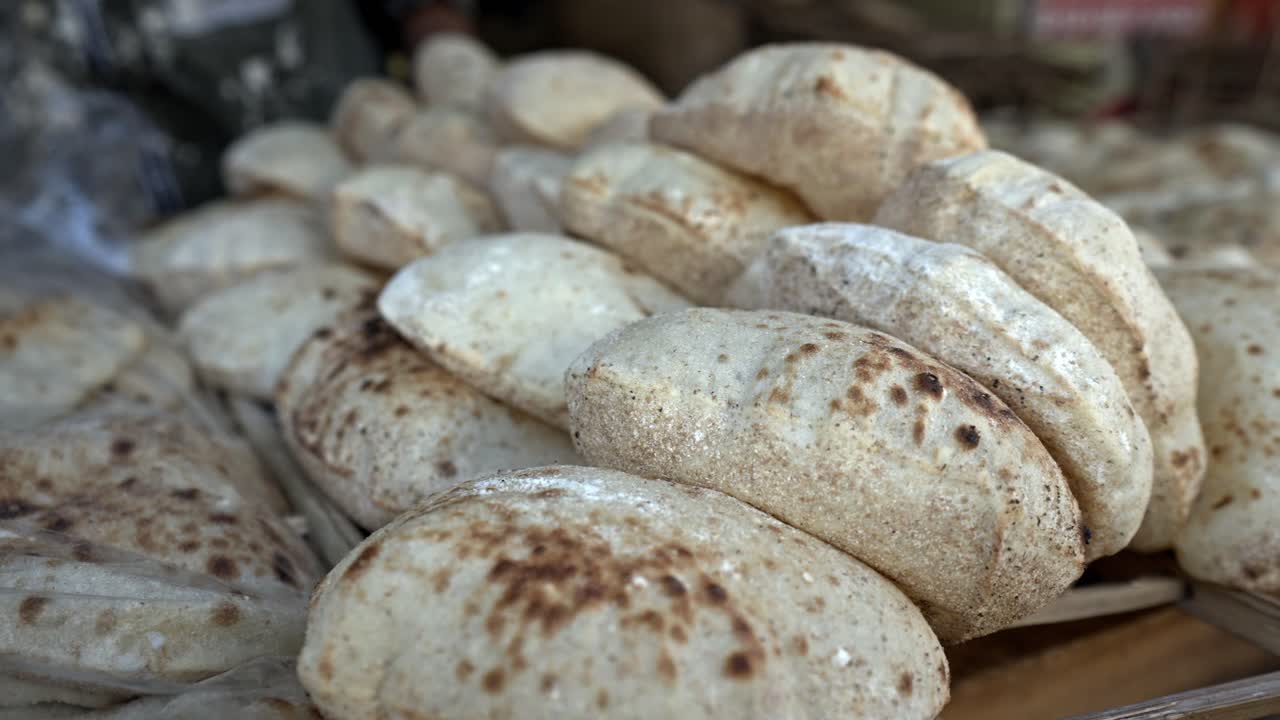 Stacks of freshly baked, puffed Eish Baladi (Egyptian flatbread) are displayed at a local market