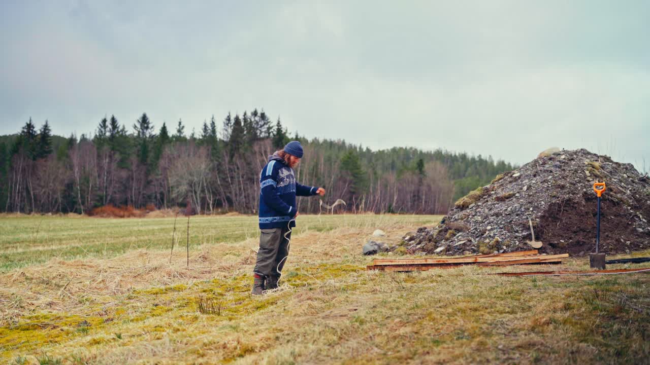 A Man Ties Rope to Charred Stakes to Outline the Field's Boundaries - Static Shot