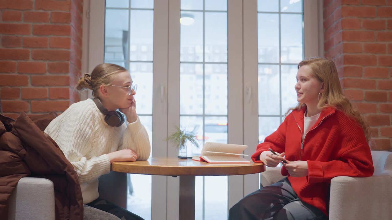 Två unga kvinnor kramar varandra och pratar på ett kafé