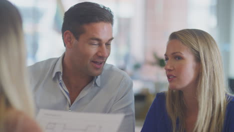 Close-Up-Of-Business-Team-Having-Meeting-Sitting-Around-Table-In-Modern-Open-Plan-Office