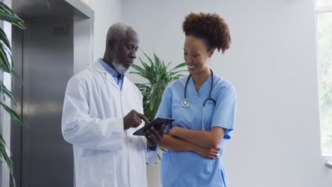 diverse female and male doctors standing in hospital discussing over tablet