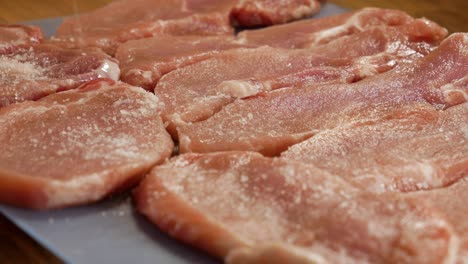 pouring salt on fresh raw pork meat steaks in close up static view