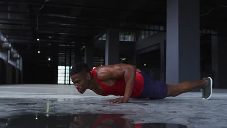 hombre afroamericano haciendo flexiones de una mano en un edificio urbano vacío