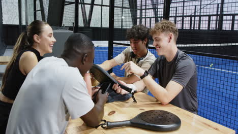 diverse friends relaxing after padel tennis match, drinks and conversation together, on indoor court