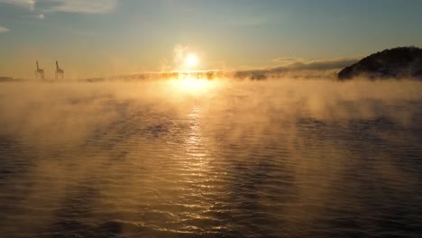 Vuelo-Bajo-Aéreo-Sobre-Olas-Con-Niebla-Flotante,-Inclínelo-Hacia-Arriba-Para-Revelar-La-Puesta-De-Sol-De-La-Hora-Dorada-Cerca-De-Bjorvika,-Oslo