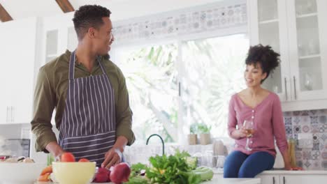 feliz pareja afroamericana cocinando y bebiendo vino en la cocina
