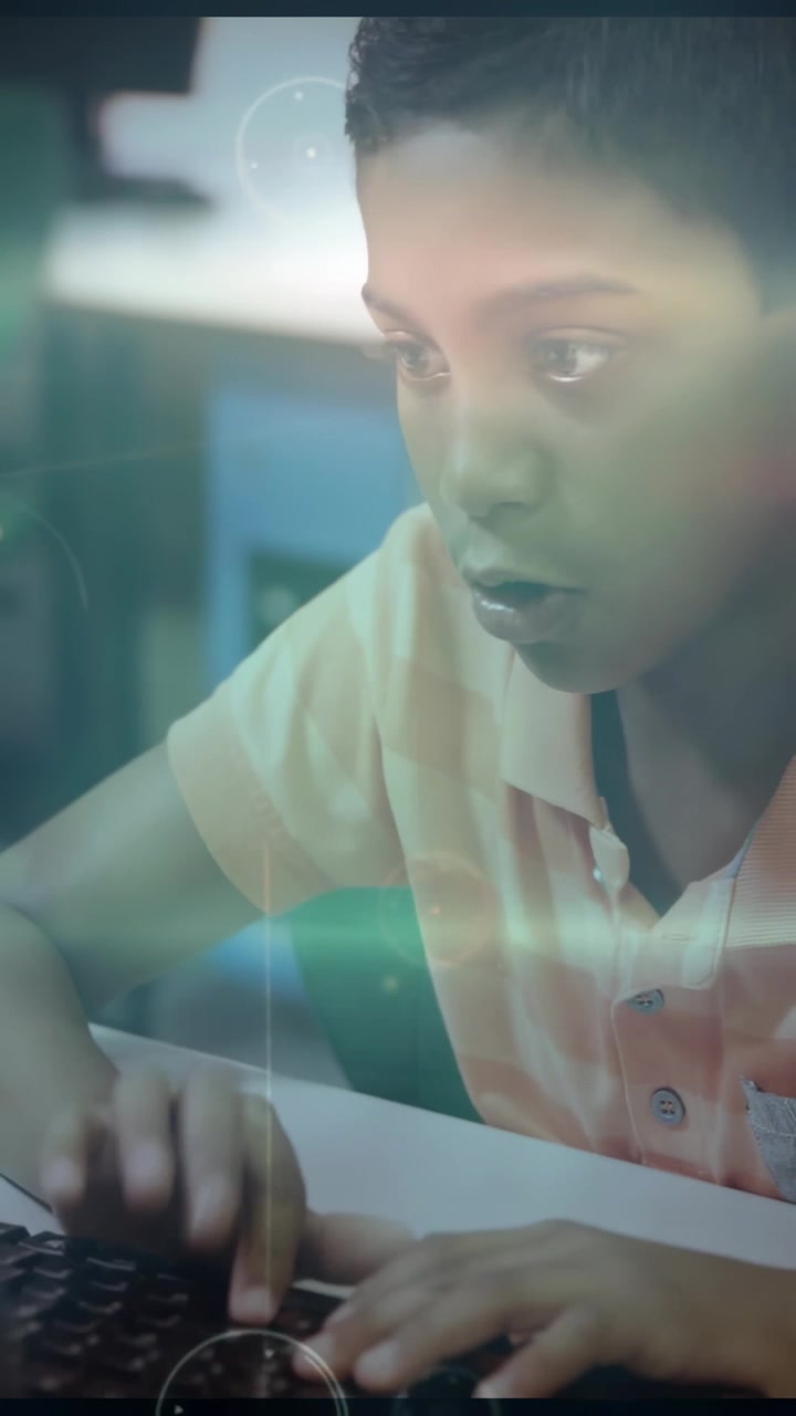 Vertical video: Boy placing hands on keys typing for school as light overlay appearing over hands