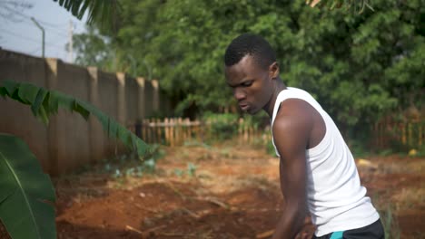 a close shot of an african man digging in his garden using a hoe in the hot sun in rural africa