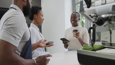 Mujer-Afroamericana-Sonriente-Pagando-Café-Para-Llevar-En-Una-Cafetería-Con-Teléfono-Inteligente,-Cámara-Lenta