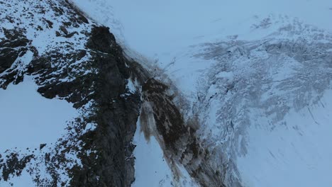 Aerial-view-capturing-a-rockfall-cascading-down-onto-the-icy-glacier-surface,-creating-contrasting-patterns