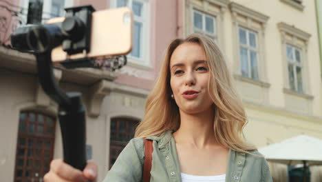 close-up view of caucasian blonde young woman recording a video on the smartphone while holding it with a selfie stick in the street