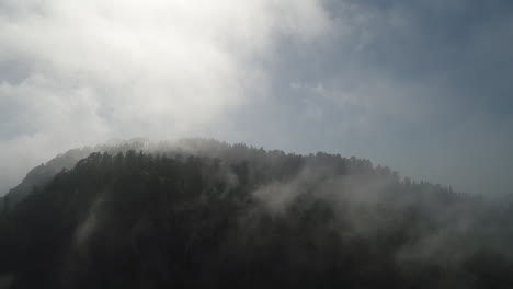 Slow-moving-drone-shot-of-fog-rolling-over-a-mountain-top