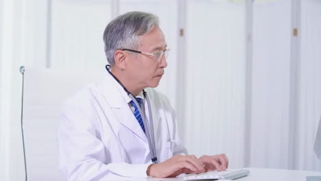 senior male doctor noting something on document and using computer in clinic