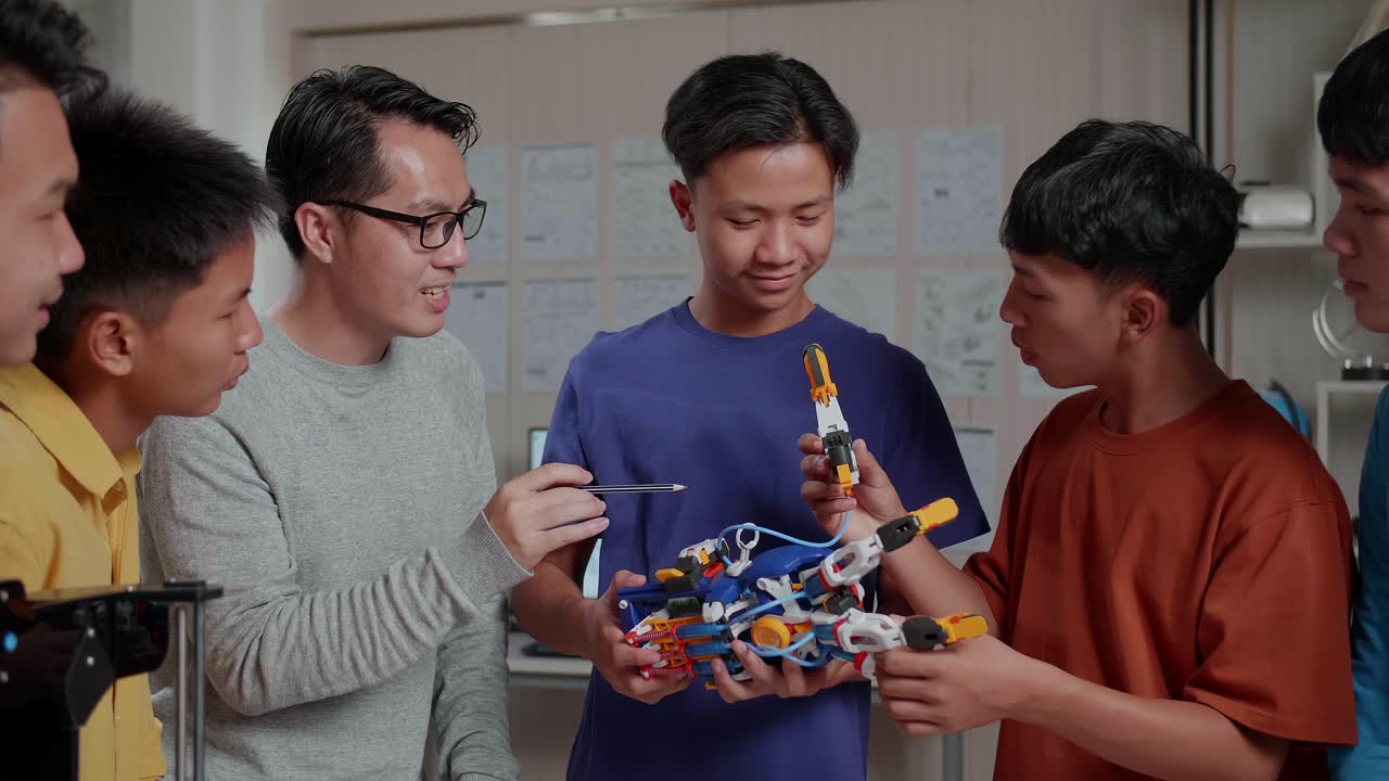 hombre asiático con una computadora portátil e impresión 3d enseñando a los niños a montar una mano de cyborg en la escuela