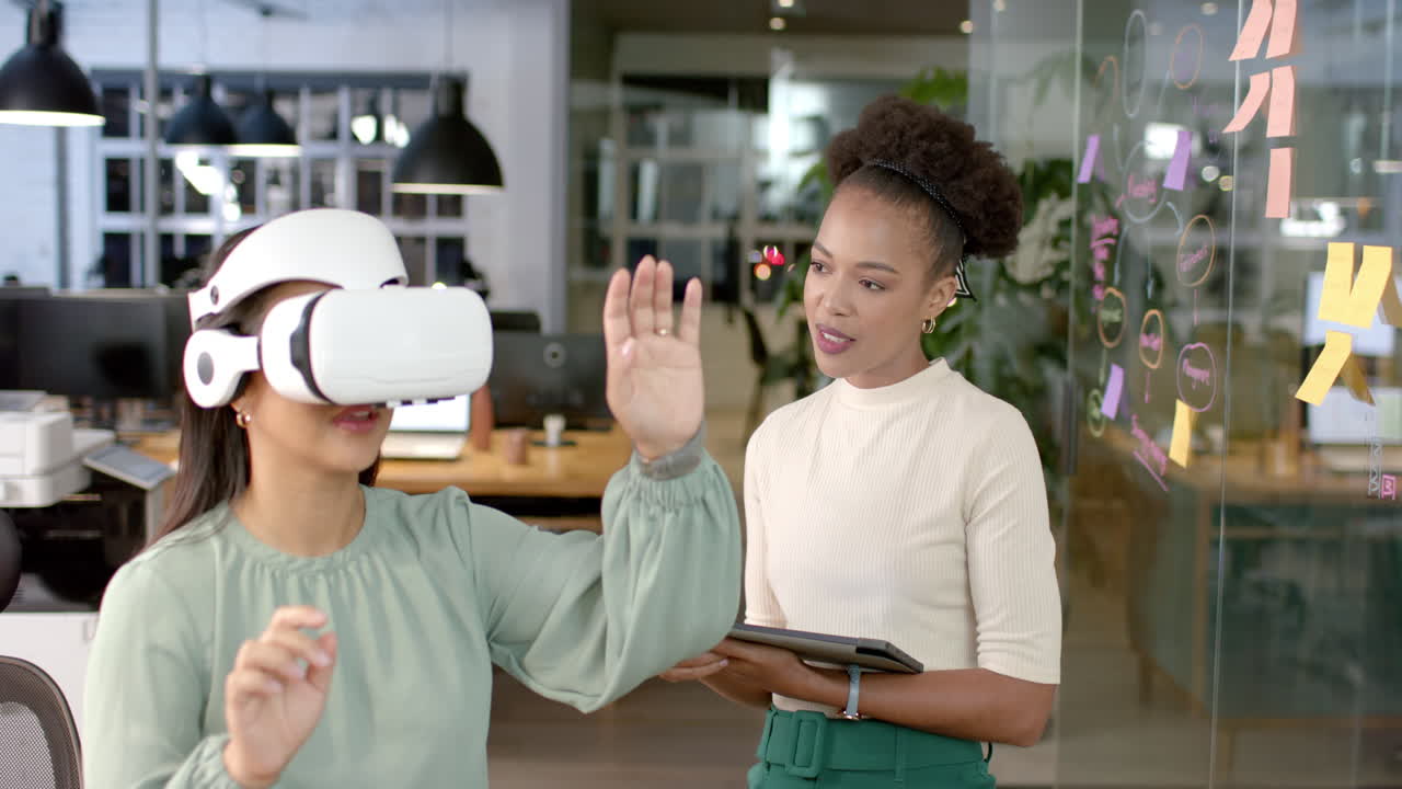 Young African American woman guides a biracial woman in a business VR experience