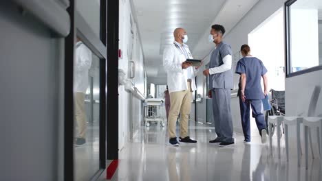 diverse doctors discussing work and using tablet in corridor at hospital, slow motion