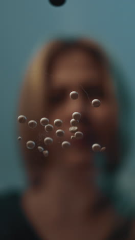 woman with health problems and medicine addiction sits at glass table with numerous scattered small tablets in semi-dark room at home close view low angle shot slow motion