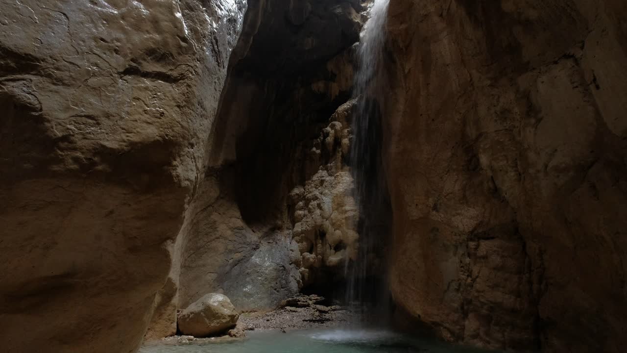 A waterfall is flowing down in a rocky canyon There is some still water at the base of the waterfall and on the canyon floor