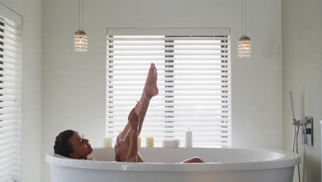 african american woman shaving her legs in the bath tub in the bathroom at home