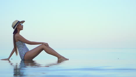 Una-Mujer-Elegante-Disfruta-Del-Mar-Cálido-En-La-Costa-Tropical,-Una-Modelo-En-Forma-Sentada-En-Aguas-Poco-Profundas,-Vista-Lateral,-Cámara-Lenta