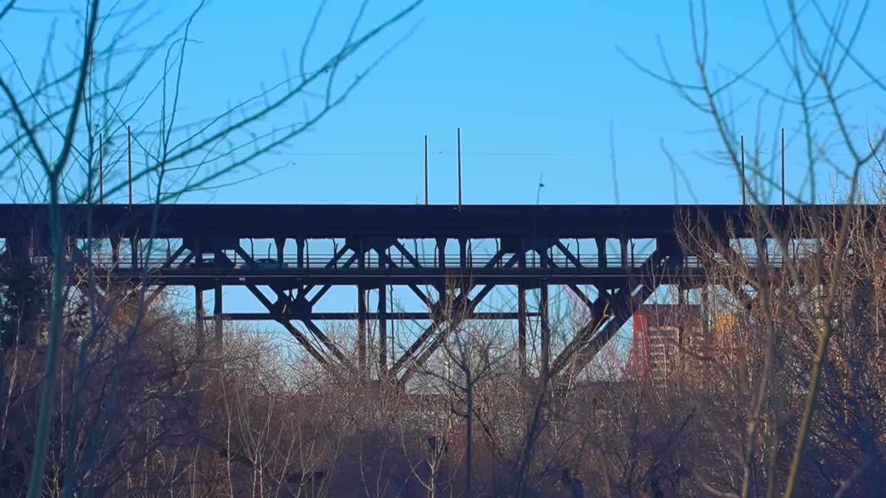 친족 공원에서 높은 수준의 강철 트러스 다리를 건너고 오래된 역사적인 육교 뒤에 건물이 있는 벌거벗은 나무 덤불 뒤를 바라보는 자동차의 그림자 실루엣