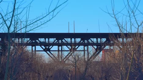 shadow silhouette of cars crossing the high level steel truss bridge vew from the kinsmen park and looking upwards behind bare branched trees bushes with buildings behind vintage historic overpass