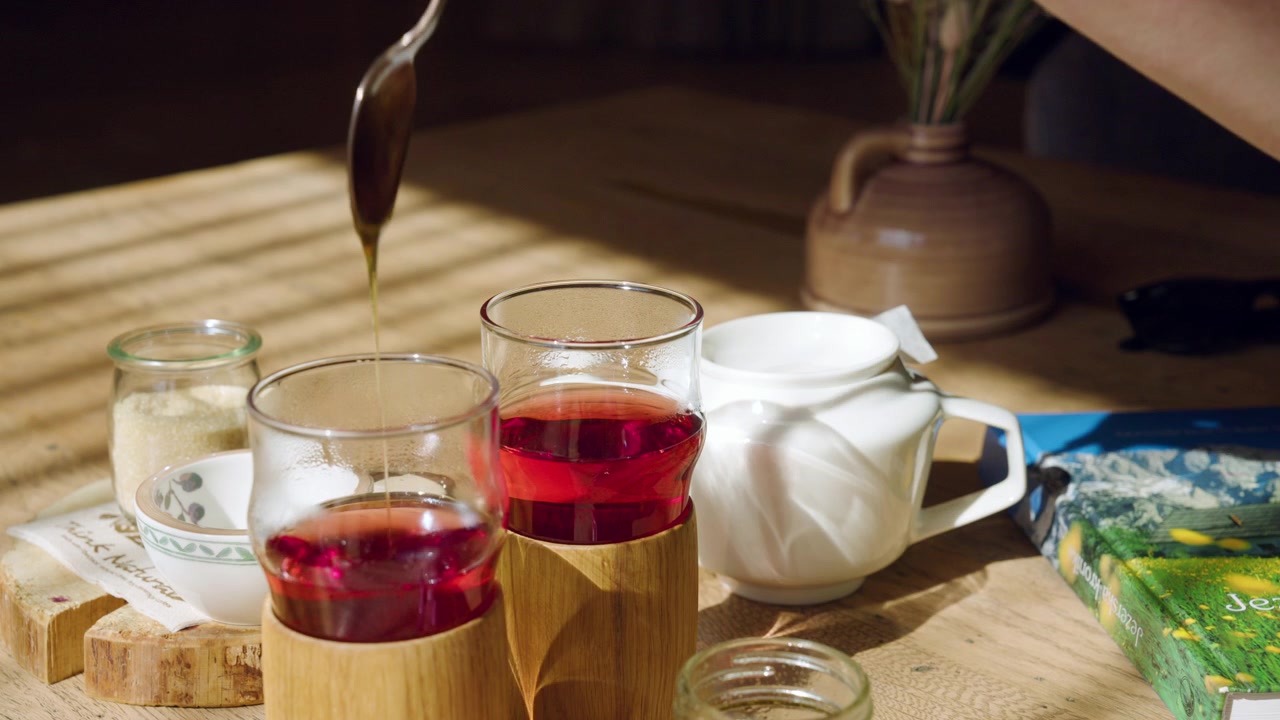Inquadratura ravvicinata di una donna che mescola il miele in una tazza di tè rosso alle erbe all'interno di una rustica baita di montagna. Primo piano.
