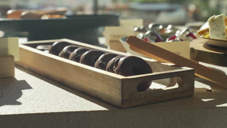 Donuts-De-Chocolate-Recién-Horneados-Presentados-En-Un-Plato-De-Madera-Durante-Un-Delicioso-Y-Soleado-Brunch-Matutino,-Creando-Una-Experiencia-De-Desayuno-Deliciosa-Y-Visualmente-Atractiva.