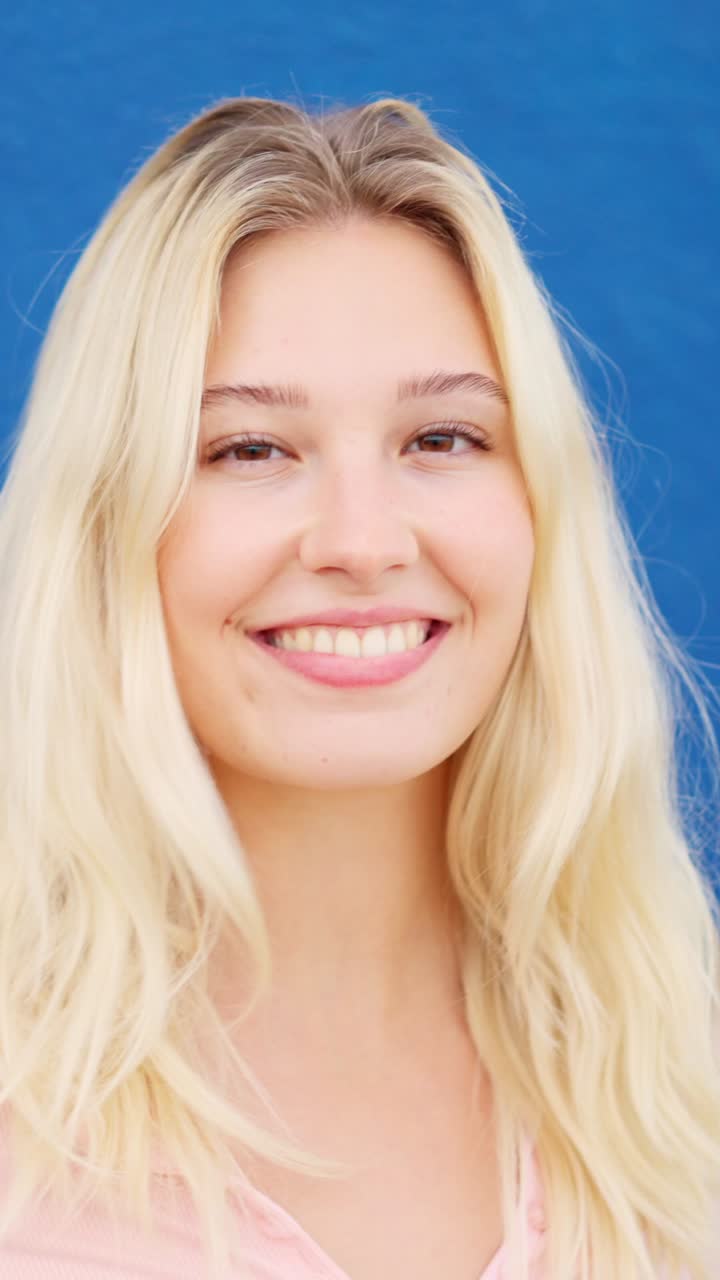 Blonde woman smiling at camera next to a blue wall