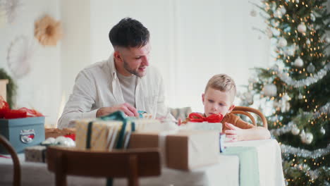 dad teaching little boy to wrap christmas presents