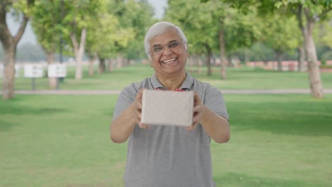 happy indian old man giving a gift in park