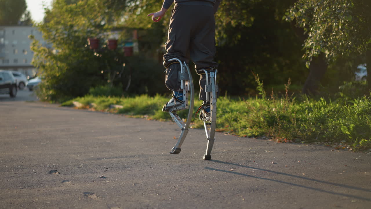 포장된 도로에서 회색 바지를 입고 발바닥으로 고 있는 사람의 하부, 초록색 잔디와 나무가 배경으로 집중된 움직임과 균형을 보여주고, 역동적인 움직임을 강조합니다.
