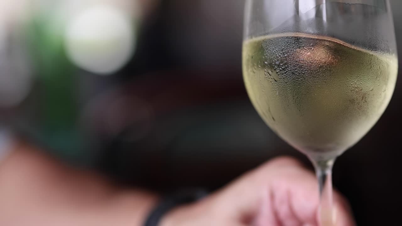 Una mano afferra un bicchiere da vino coperto di condensa, riempito con vino bianco freddo.