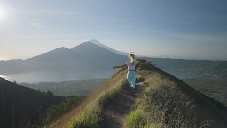 young female athlete running on mountain ridge in bali spreading arms, concept of freedom