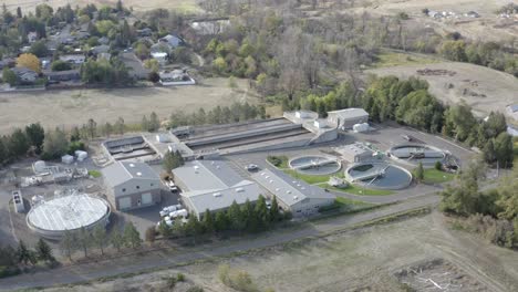 Aerial-view-rotating-shot-taken-from-a-drone-of-pools-of-water-and-buildings-at-a-water-treatment-plant-on-the-outskirts-of-a-town-on-a-bright-sunny-day