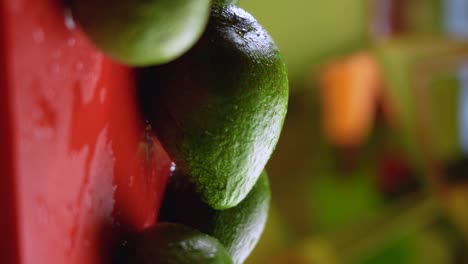 An-avocado-on-a-red-cutting-board-falling-from-above-among-a-group-of-avocados-in-slow-motion-